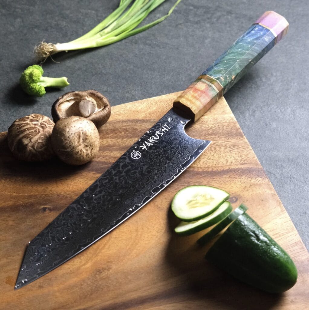 A wooden cutting board with a Japanese Damascus knife and vegetables on it.