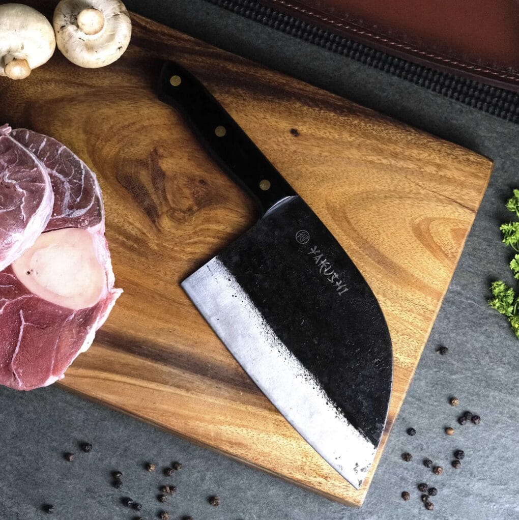 A Japanese Damascus Butcher knife on a cutting board with meat on it.