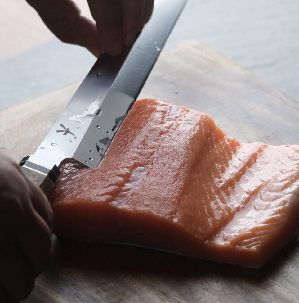 Chef slicing a raw salmon fillet on a cutting board with a LEGENDARY Damascus Fillet Knife.