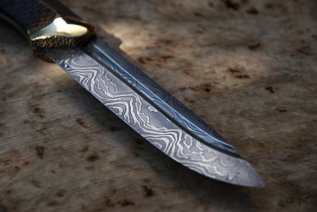 A close-up of a damascus steel knife, renowned for its durability, with a patterned blade and textured handle, resting on a wooden surface.